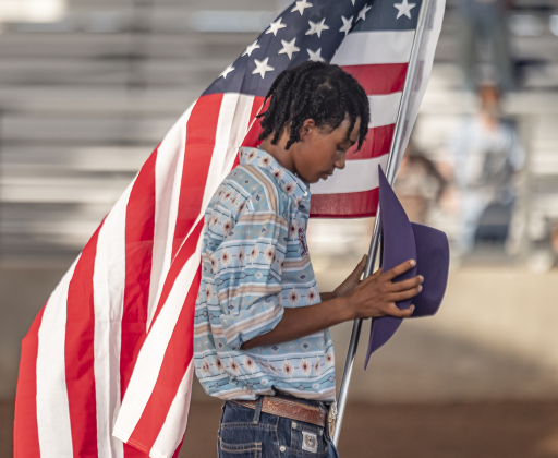 16-year-old Jacki Gayle, a bull rider (the only female bull rider on this evening) from Odessa, Texas, presents the American flag in the arena at the start of  the Bill Pickett Youth Rodeo, held at the Williamson County Expo Center  on Saturday, June 21, 2025.  Now in its second year, the rodeo showcases athletes 18 or younger. The event is coordinated by the Bill Pickett Youth Rodeo Association.     Photo by Andy Sharp.