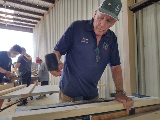 Bill Booth hammers place-holding holes, before passing the pine board along for holes to be drilled in a bed’s headboard.