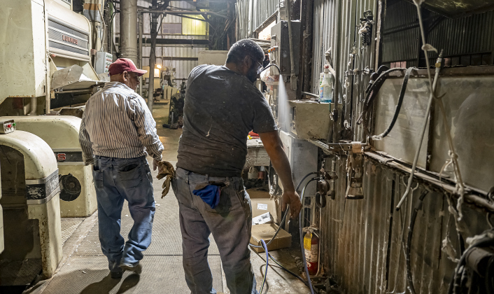 Felix Valdez sprays off excess cotton at the end of the day’s work at Waterloo Gin on Tuesday, September 9, 2025.  Tony Espinoza is at left.  The gin is along County Road 414 east of Taylor.   Photo by Andy Sharp.