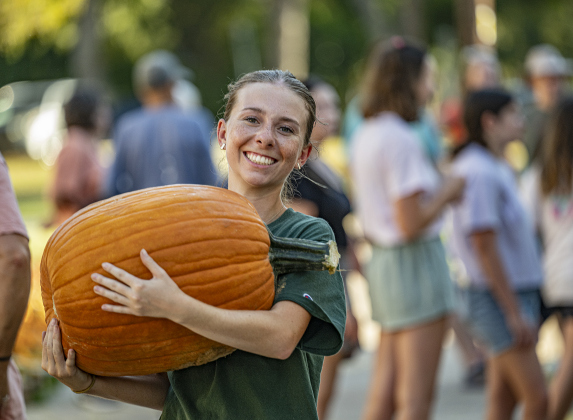 Southwestern University freshman Emily York totes one of  more than 3,000 pumpkins at Georgetown First United Methodist Church on Wednesday afternoon, October 8, 2025.  Church members and volunteers from area high schools, plus students from Southwestern University helped  place the pumpkins.  46,000 pounds of pumpkins arrived here from the Navajo Nation in New Mexico.  The pumpkins will be available until Halloween.   Photo by Andy Sharp.