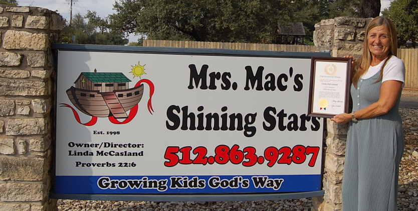 Linda McCasland stands with her Yellow Rose of Texas award in front of the sign for Mrs. Mac’s Shining Stars Preschool, the business she owns. (Photo by Kaitlyn Wilkes)