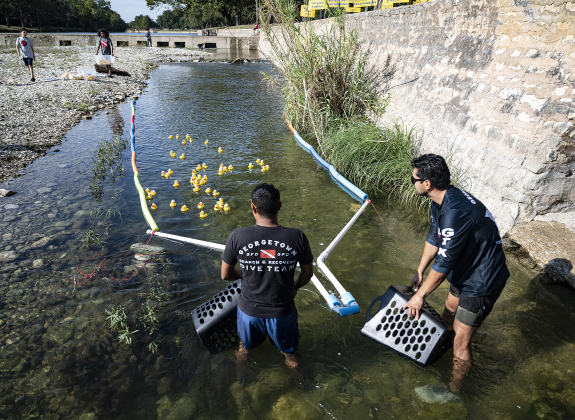 Pablo Felix, left, and Jonathan Marquez, right, members of the Georgetown Police Department Dive Team, prepare to gather rubber ducks nearing the finish line during  the 10th Annual AAUW Duck Race held on the river at San Gabriel Park on Saturday, November 1, 2025.  Rubber ducks are placed in the river and race to the finish in several heats.  Winners of winning ducks win prizes.   The event raises funds for area high school student scholarships. Photo by Andy Sharp. 