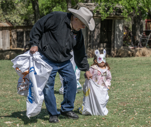 Williamson Museum volunteer Bob Brownwood, left, helps 4-year-old Celeste Gualtieri navigate the course during a sack race  at the Old Settlers Association  site during The Williamson Museum’s Hoppy Easter event on Saturday, March 14, 2026.
