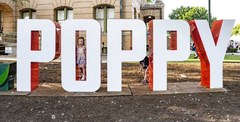 4-year-old Iris Vinson enjoys time with the large “Poppy” letters along 8th Street on the courthouse lawn on Friday, April 24, 2026, , the first night of the Red Poppy Festival.    Photo by  Andy Sharp.
