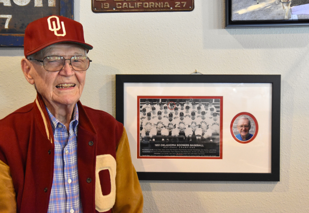1951 University of Oklahoma baseball player Bill Harrah stands next to his team photo featured in Wriggley’s Pub in Sun City. It was during this season the team won the school’s first baseball national championship. Mr. Harrah is circled in the team photo, third row from the bottom, third from the left. The letterman jacket and hat are from his student days. (Photo by Kaitlyn Wilkes)