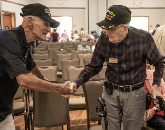 World War II Navy veteran Cliff McCrummen, left, who will be 100-years-old on June 23rd, shakes the hand of World War II Air Force veteran Ralph May, right, who will be 99 in two weeks, during  during the Memorial Day ceremony held in Sun City on Monday, May 25, 2026.  The chance of rain moved this year’s ceremony inside the Sun City Social Center ballroom, filled to capacity with several hundred attendees.   Photo by Andy Sharp.
