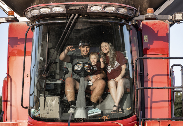 Montgomery Raesz, his wife Madalynn and their daughter Maizlee, 16-months-old, prepare to guide a combine through a field of corn along County Road 101 during the 2026 corn harvest of brothers Shaun and Steven Raesz on Saturday, July 11, 2026.  Montgomery, 26,  is the first-born son of Shaun Raesz and his wife Kari.   The family is harvesting over 4,000 acres of corn this season.     Photo by Andy Sharp