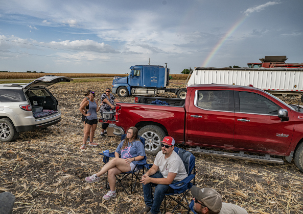 A rainbow forms in the distance as workers take a supper break during the corn harvest of brothers Shaun and Steven Raesz con Friday, July 10, 2026.   In the red cap is Maverick Raesz, Shaun’s son, joined his fiancee Mikala.  The couple are getting married in October.  These East Williamson County farmers are harvesting over 4,000 acres of corn this year.    Photo by Andy Sharp