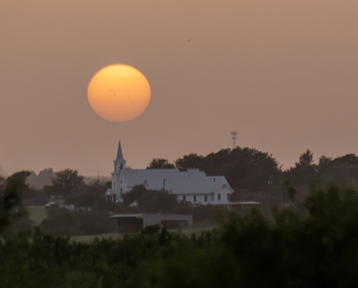 A hazy sunset approaches over St. Peter’s Church of Coupland on Monday, June 29, 2026.  Central Texas, and areas of the south and southwest United States are beginning to experience Saharan Dust during the early-summer days.   Photo by Andy Sharp