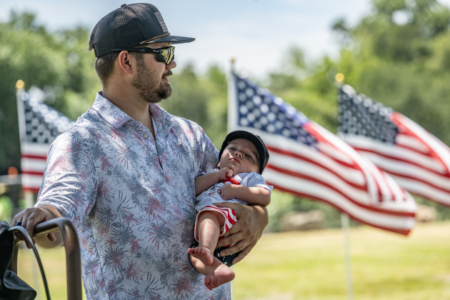 Houston McFarlane and Brantley, his relaxed four-month-old son  found a shady spot to beat the afternoon heat during the Sertoma Club 4th of July celebration in San Gabriel Park on Saturday, July 4, 2026. The flags in the background were brought by the Rotary Club of Georgetown.    Photo by Andy Sharp