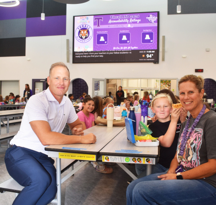 Thrall ISD Interim Superintendent Blake Schneider, Thrall Elementary School principal Sherri Maruska, and students Bree Guajardo, left, and Prestly Pehl, celebrate the school’s third “A” state rating at lunch. A marquee touts the great news.  Photo by Katherine Hamilton