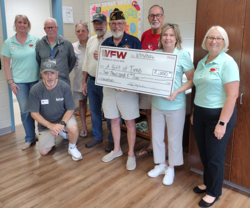 Georgetown VFW Post 8587 Commander and Navy veteran John McCleskey presents Gift of Time Executive Director Becky Folta-May with a $2,000 check Aug. 25. Navy veteran John Gulling, a musician with Fond Memories, is kneeling.  Pictured in the back row are Activities Director Jeanette Workman, respite participant and Air Force veteran Rusty Lowe, Fond Memories musician Terry Aynes, visitor and Coast Guard veteran John Bowen, Fond Memories musician Ty Choate and Gift of Time Board President Mary Odom.