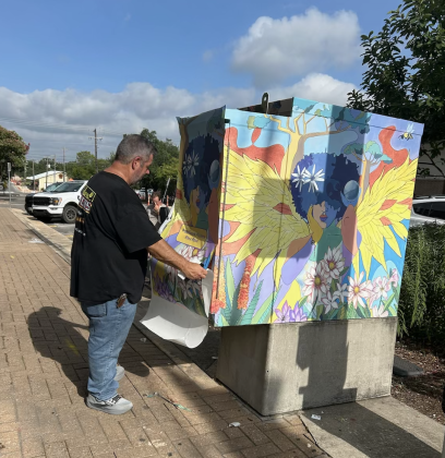 Neil Lanning installs “Patchwork Phoenix” on the corner of Austin Avenue and Seventh Street on July 29. He installed the previous utility box art pieces eight years ago when they were first displayed. (Photo by Linda Fenton)