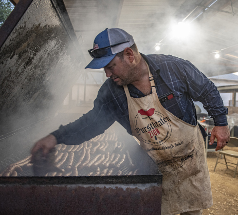 John Faske checks on the progress of sausages being smoked in one of several large pits. Approximately 12,600 pounds of sausage were prepared and smoked this year at the church.