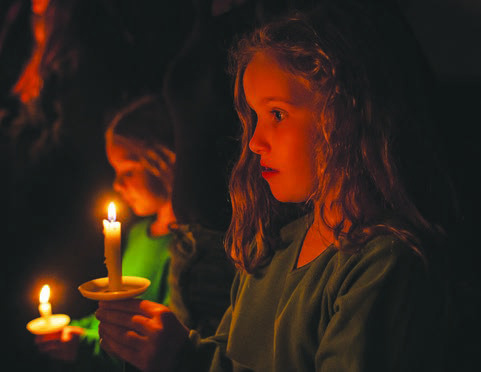 Freya Crenshaw, 8, and her sister Zinnia, 6, (back left) hold onto their candles during the singing of “O Come, All Ye Faithful.”