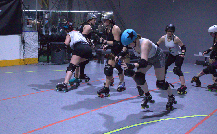 Meghan Sammons, who goes by Goldie when playing roller derby, wears a blue helmet covering called a pantie and skates through the blockade. Photo by Nalani Nuylan.