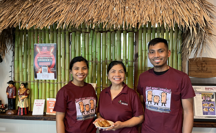 Elsie Corass, owner of Elsie’s Egg Rolls in Hutto, stands holding an eggroll order next to her two children, Reina Lamberton and Eugene Trinidad. The order counter behind them is modeled after a traditional Nipa Hut. Photo by Abbey Archer