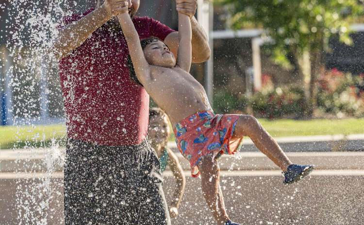 Jose Rogel swings his son Maximillian, 4, through the water while daughter Luna, 5, looks on  during a visit to the splash pad at Heritage Square Park on Tuesday, June 17, 2025.  The official beginning of summer is Friday, June 20th, but Williamson County residents have been seeking respite for a while.