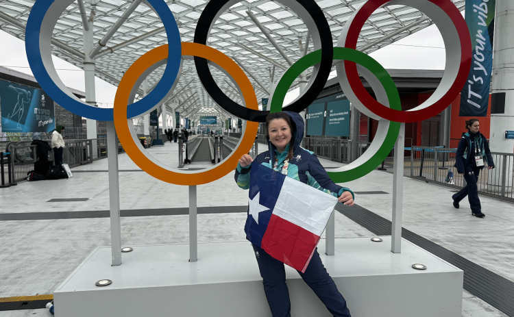 Leander resident Anna Yelaun stands in front of the Olympic rings holding a Texas flag. Ms. Yelaun volunteered at the 2026 Milan Cortina Winter Olympics as the lead volunteer for speed skating. (Photo courtesy Anna Yelaun)