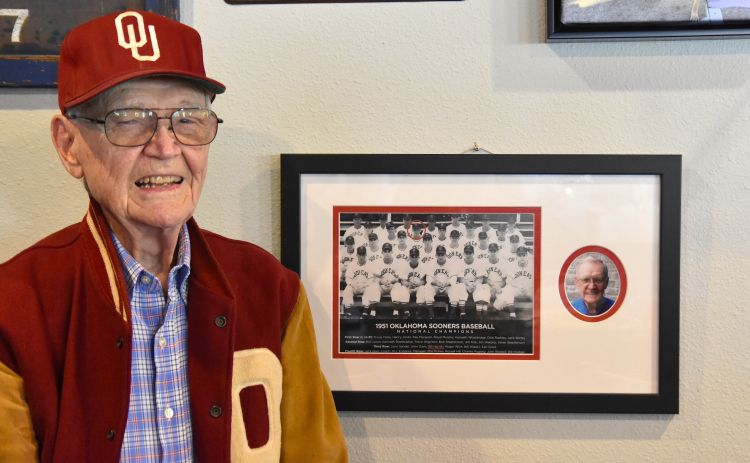 1951 University of Oklahoma baseball player Bill Harrah stands next to his team photo featured in Wriggley’s Pub in Sun City. It was during this season the team won the school’s first baseball national championship. Mr. Harrah is circled in the team photo, third row from the bottom, third from the left. The letterman jacket and hat are from his student days. (Photo by Kaitlyn Wilkes)