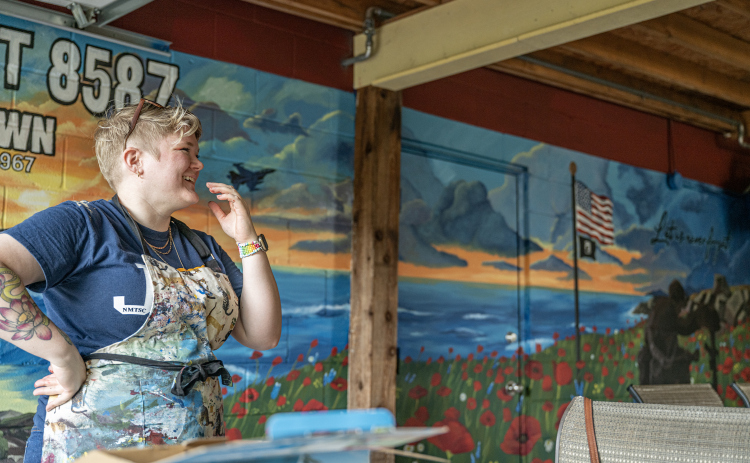 Artist Shelby Gage smiles  Friday, August 14, while she puts finishing touches on a VFW mural she created for Msg. Ben D. Snowden Post 8587. Last steps included adding a clear coat to protect her work.