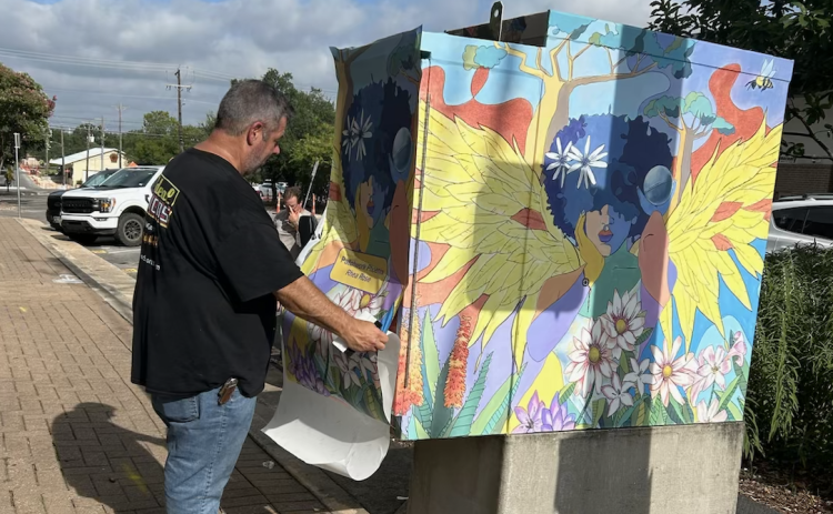 Neil Lanning installs “Patchwork Phoenix” on the corner of Austin Avenue and Seventh Street on July 29. He installed the previous utility box art pieces eight years ago when they were first displayed. (Photo by Linda Fenton)