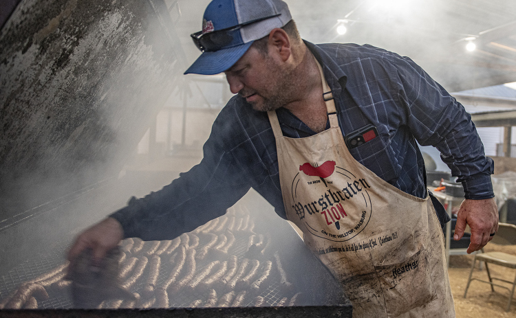 John Faske checks on the progress of sausages being smoked in one of several large pits. Approximately 12,600 pounds of sausage were prepared and smoked this year at the church.